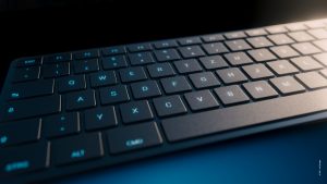 Nahaufnahme einer Tastatur mit dunklen flachen Keycaps und blau leuchtenden Buchstaben