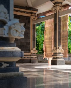 Ein leerer Tempel auf Bali mit einem wehenden Sonnenschutz und spiegelglattem Boden